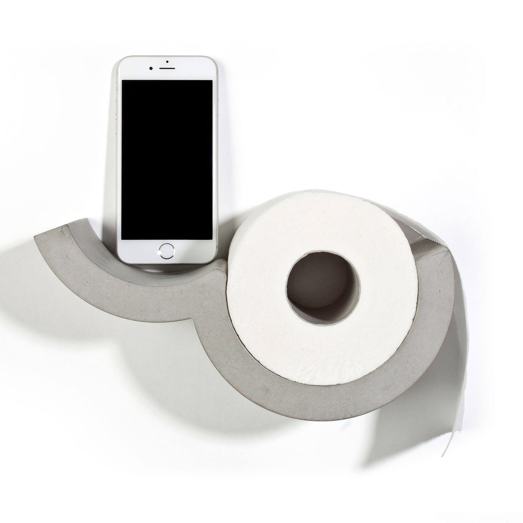 Designer bathroom toilet paper dispenser in concrete holding one roll and a smartphone. 