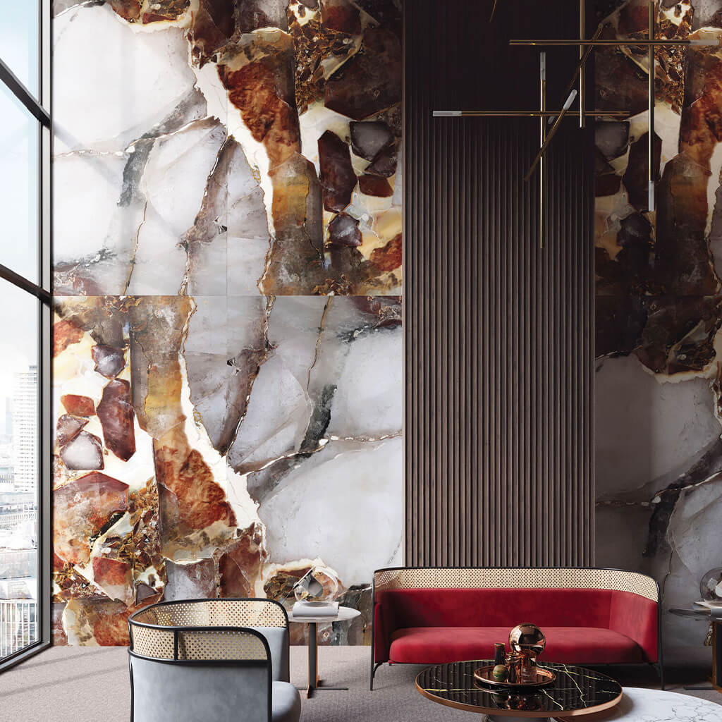 The Papetta wall panel is installed in a luxury high-rise building. The image shows 2 designer sofas in red and gret with a marble coffee table. and luxury gold lighting. Behind is our Papetta wall panels in the marble and precious stone design.