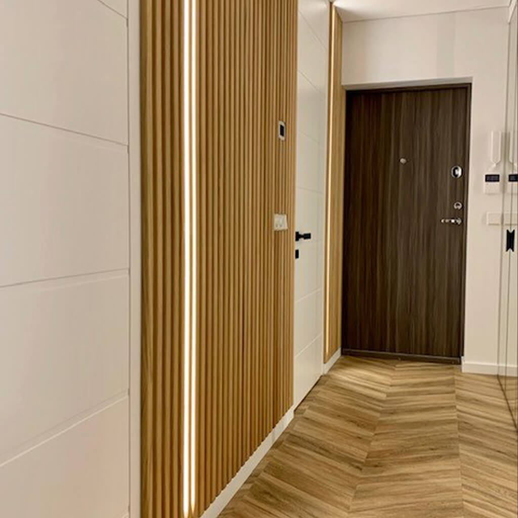 An office wall and door. The wall has been clad with the fluted wall panels and there is 2 led light strips installed in-between some of the flutes. 
