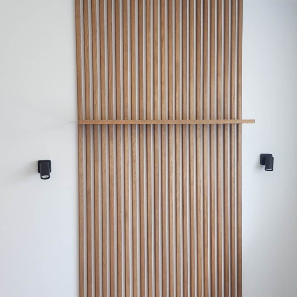 A section of white wall with the flutes installed. A shelf in a similar  wood finish has been added onto the panels.